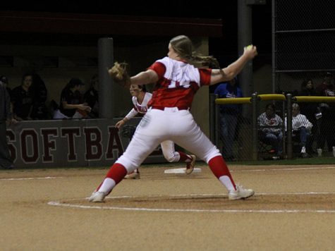 Carter Spex (#14) pitching with Katherine Thompson in the background.