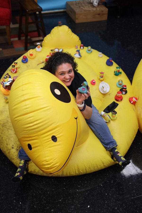 Forensics teacher Diana Martinez poses in a duck shirt and socks, with her rubber ducks all on a giant inflatable duck.